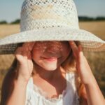 Fetiță purtând pălărie și ascunzându-se de soare